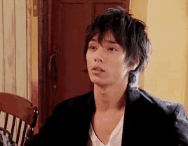a young man in a black jacket and white shirt is sitting in a chair in front of a door .