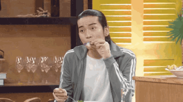 a man with long hair is eating something with a fork and spoon