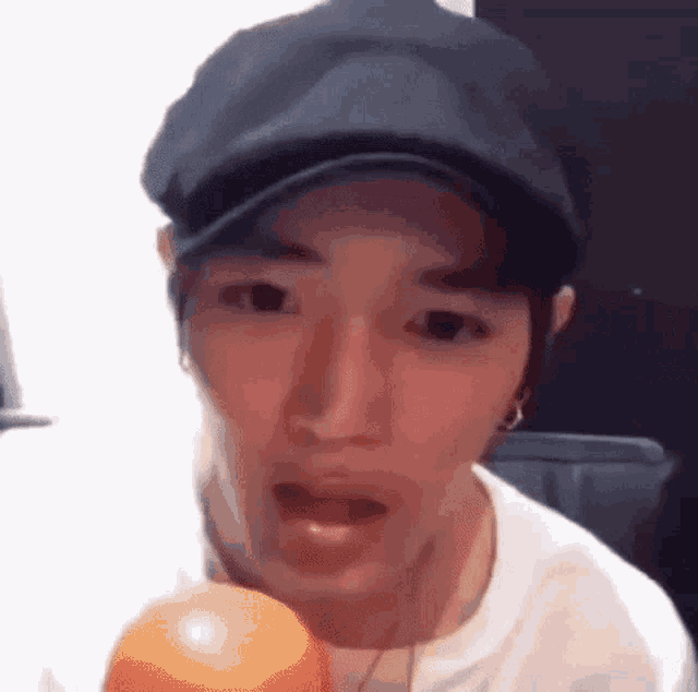 a man wearing a hat and a white shirt is holding an orange in his hand .
