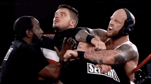 a group of men are wrestling in a ring and one of them is wearing a headset .