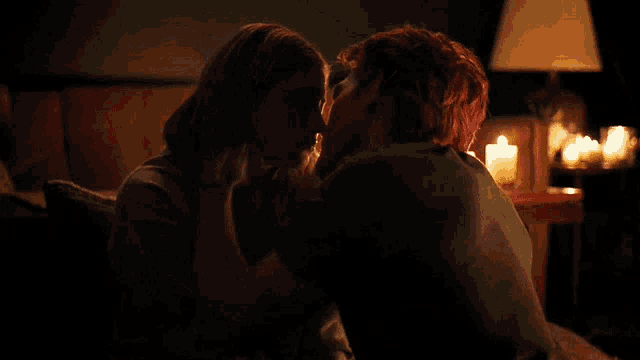 a man and a woman are kissing in a dark room with candles