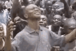 a man in a blue shirt is standing in front of a crowd of people with his arms in the air .