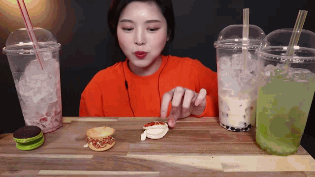 a woman in an orange shirt is eating a sandwich next to two cups of drinks