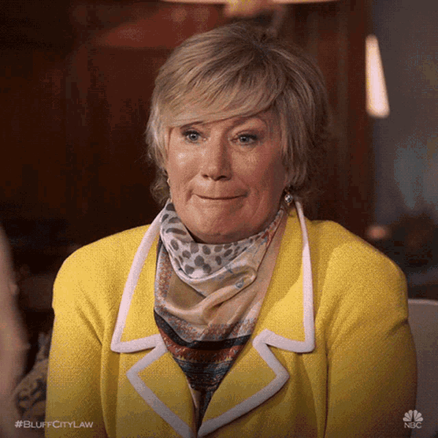 a woman wearing a yellow jacket and a scarf is sitting on a couch
