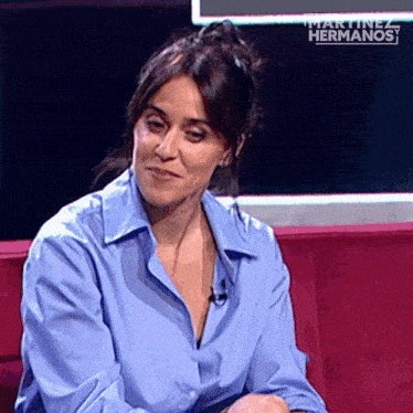a woman in a blue shirt is sitting on a pink couch with the words martinez hermanos on the bottom