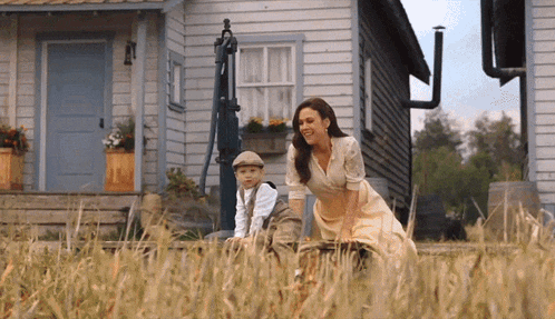 a woman and a boy are sitting in a field in front of a house
