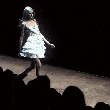 a woman in a white dress is walking down the runway at a fashion show