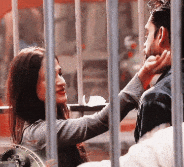 a woman is touching a man 's face behind bars with a clock in the background