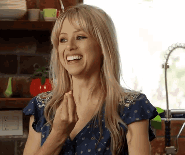 a woman in a blue shirt is smiling and making a heart shape with her hands .