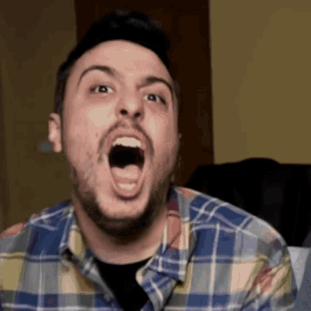 a man in a plaid shirt is making a funny face with his mouth open