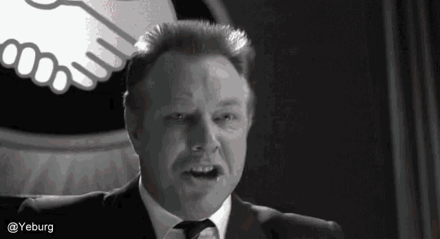 a man in a suit and tie is giving a speech in front of a handshake logo