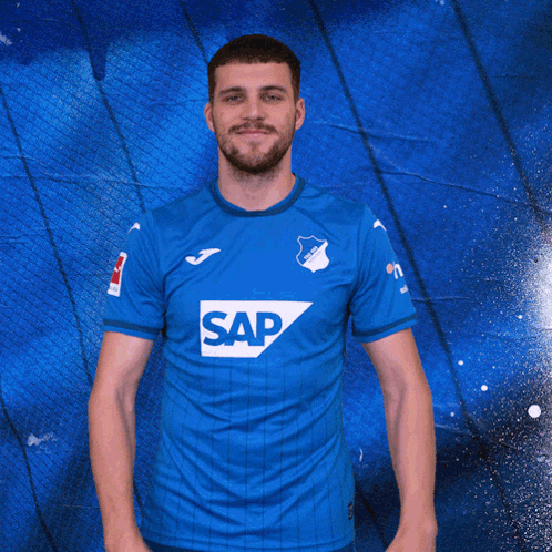 a man wearing a blue shirt with the word sap on it makes a heart shape with his hands