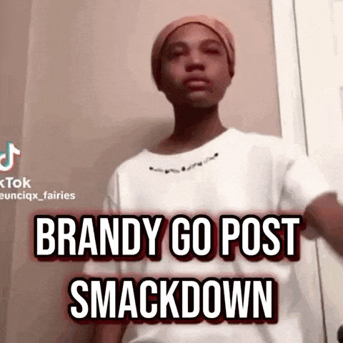 a young man wearing a hat and a white shirt is standing in front of a door and says brandy go post smackdown