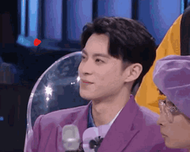 a man in a purple suit is sitting next to another man in a purple hat in front of a microphone .