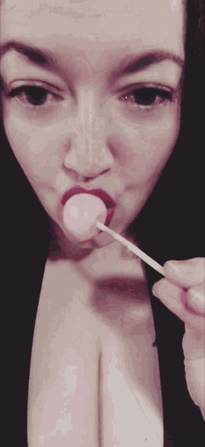 a woman is licking a pink lollipop with red lips