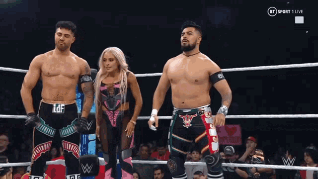 two men and a woman are standing in a wrestling ring with a sign that says i love you