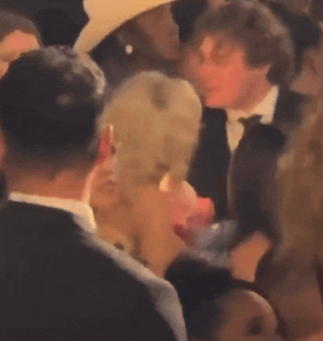 a man in a suit and tie is talking to a woman in a hat at a party .