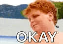 a man with red hair is standing in front of a body of water with the words `` okay '' written on it .