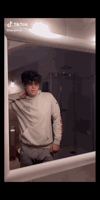 a young man standing in front of a mirror with tiktok written on the bottom of the screen