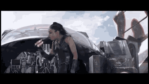 a woman in a black costume is standing in front of a futuristic vehicle .