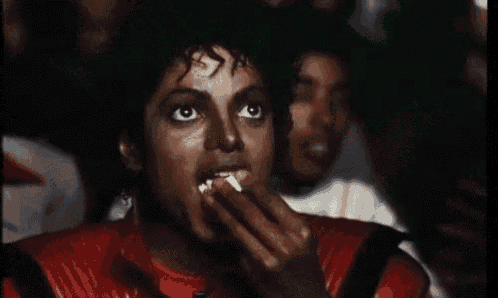 a man in a red leather jacket is eating popcorn in a crowd of people .