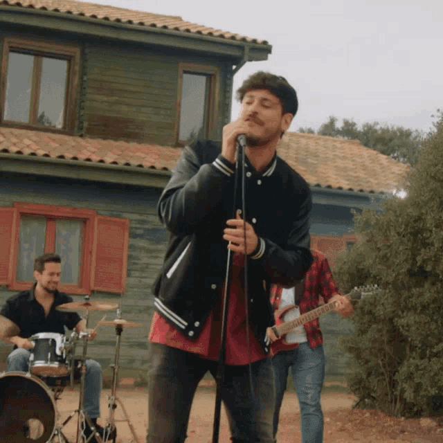 a man singing into a microphone in front of a drummer and a guitar player