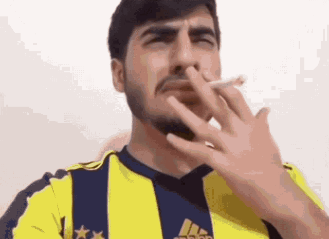 a man with a beard is smoking a cigarette and wearing an adidas shirt