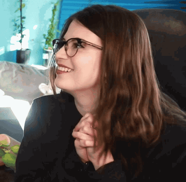 a woman wearing glasses and a black shirt smiles with her hands folded