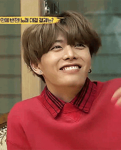 a young man wearing a red shirt is smiling in front of a sign that says ' ? '
