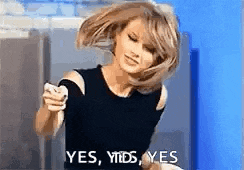 a woman in a black top is holding a cell phone and says yes , yes , yes .