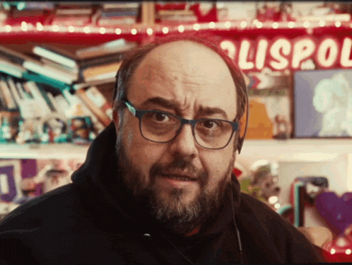 a bald man with glasses and a beard is standing in front of a sign that says lispol