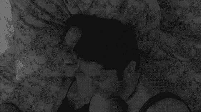 a man and a woman are kissing in bed in a black and white photo .
