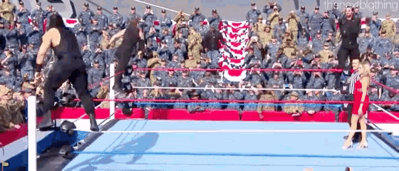two men are wrestling in a ring with a crowd of soldiers watching .