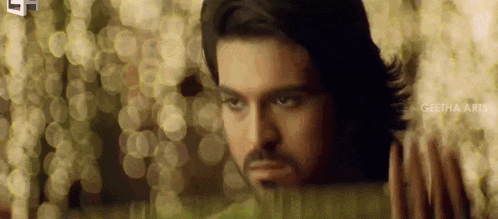 a man with long hair and a beard is standing in front of a window .