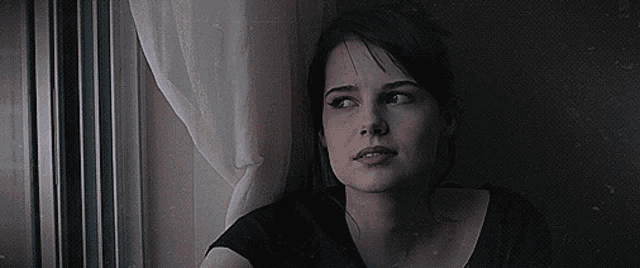 a woman looking out of a window with a white curtain