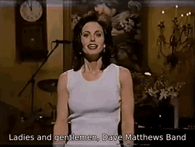 a woman in a white tank top is singing into a microphone while standing in front of a microphone .