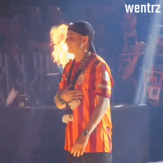 a man in an orange and red striped shirt is holding a flaming object in his mouth and the word wentrz is on the bottom