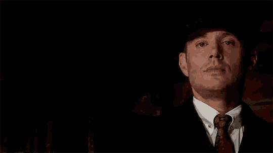 a man in a suit and tie is wearing a hat and tie in the dark .