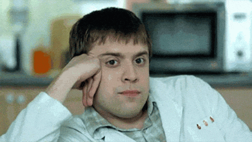 a man in a white lab coat is sitting with his hand on his head .