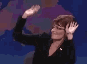 a woman in a black suit and glasses is raising her hands in the air