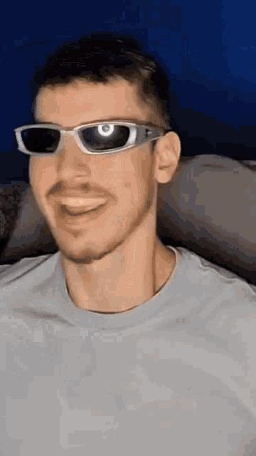 a man wearing sunglasses and a grey shirt is smiling .