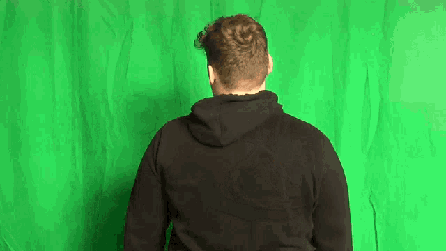 a man in a black hoodie stands in front of a green screen