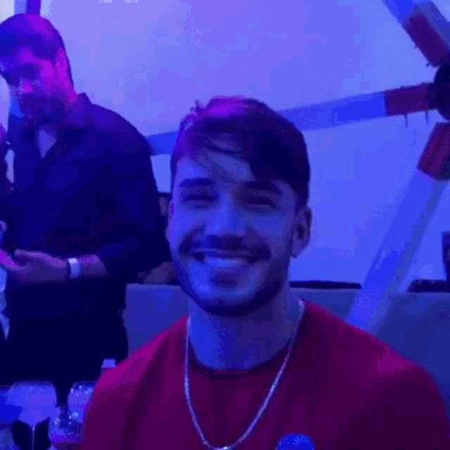 a man with a beard wearing a red shirt is smiling in a dark room