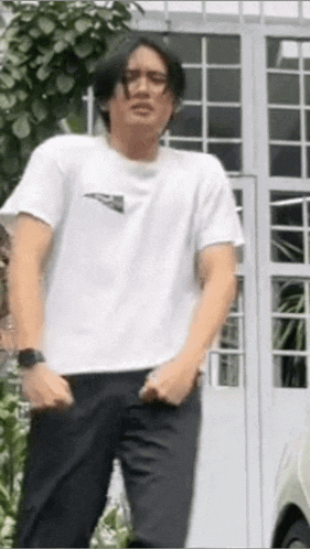 a man wearing a white t-shirt and black pants is standing in front of a white building .