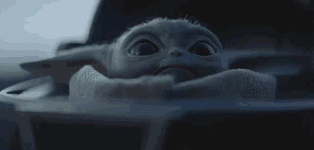 a baby yoda is laying in a blanket in a crib and looking at the camera .