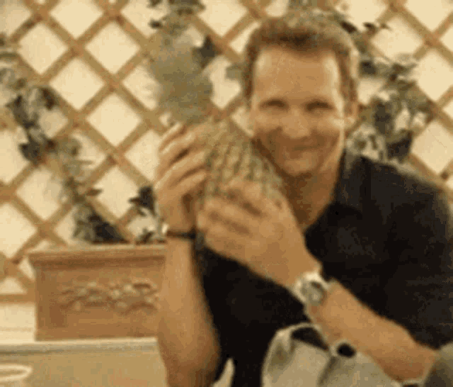 a man in a black shirt is holding a pineapple in his hands and smiling