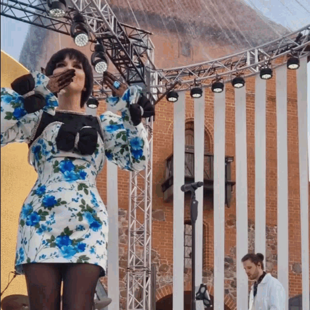 a woman in a blue and white floral dress stands in front of a microphone