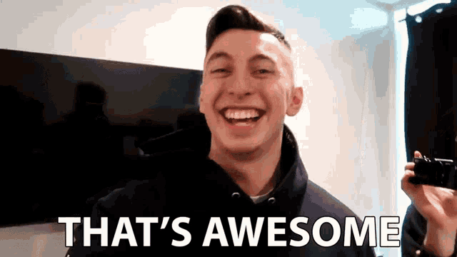 a man is smiling and holding a camera with the words that 's awesome written below him