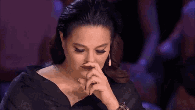 a woman in a black dress is holding her nose with her finger .