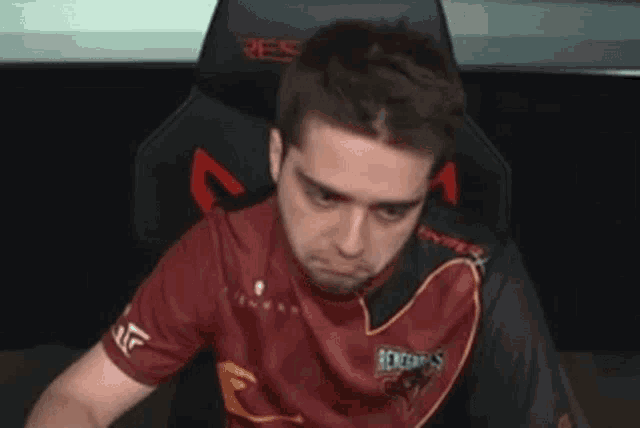 a man in a red shirt is sitting in a chair with his head down .